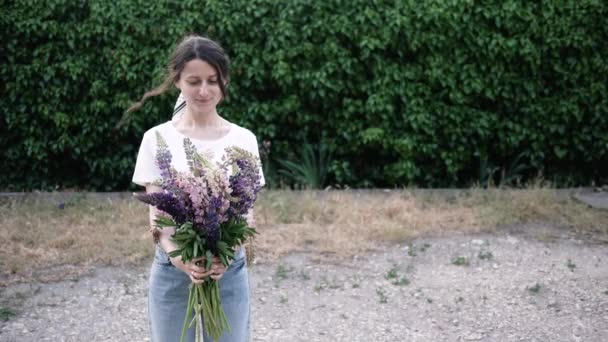 아름다운 젊은 여자가 꽃다발을 들고 푸른 잎사귀 벽 가까이에 서 있는 냄새를 맡는다. 꽃 사업의 개념, 꽃 과 관련된 일. 4K — 비디오