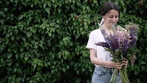 Kamera soldan sağa, yapraklardan oluşan yeşil duvar boyunca elinde bir buket çiçekle genç bir kadına gidiyor. — Stok video