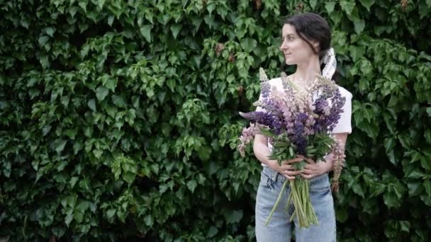 푸른 잎으로 된 벽 가까이에 꽃 다발이서 있는 아름다운 젊은 여자. 꽃 사업의 개념, 꽃 과 관련된 일. 복사 공간. 4K — 비디오