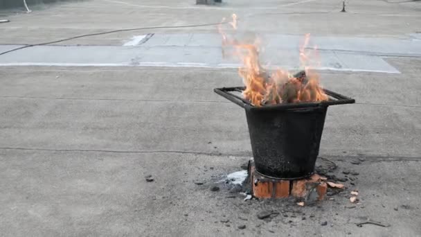 The bitumen melted on the bucket by fire for roofing roof repair — Stock Video