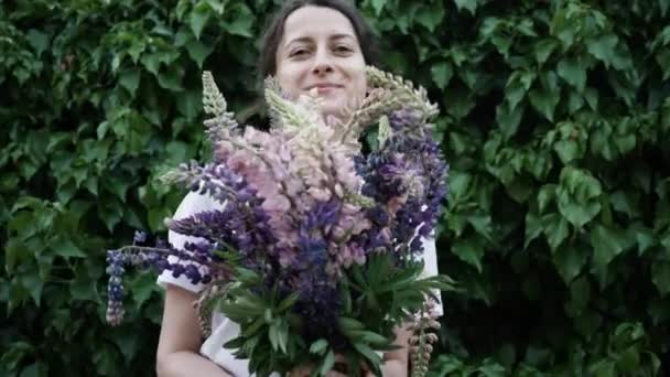 Красива молода жінка тримає букет квітів перед собою, намагаючись виглядати над букетом. 4-кілометровий — стокове відео