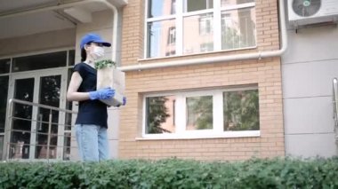 Kurye, koruyucu maskeli kurye ve tıbbi eldivenli teslimatçı paket yemek getiriyor. Karantina altında teslimat hizmeti, hastalık salgını, koronavirüs covid-19 salgını. Evde kal.