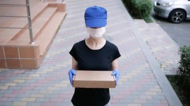 Postacı, koruyucu maskeli kurye ve tıbbi eldiven taşıyan küçük bir paket taşıyor. Karantina altında teslimat servisi, salgın hastalıklar. Sosyal uzaklık kavramı