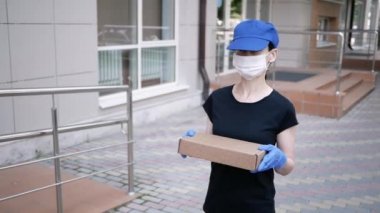 Postacı, koruyucu maskeli kurye ve tıbbi eldiven taşıyan küçük bir paket taşıyor. Karantina altında teslimat servisi, salgın hastalıklar. Sosyal uzaklık kavramı