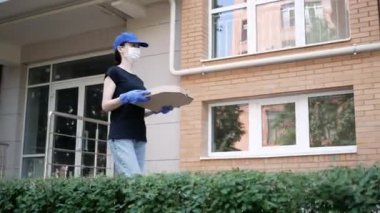 Kurye, koruyucu maskeli kurye ve tıbbi eldivenli teslimatçı paket pizza getiriyor. Karantina altında teslimat hizmeti, hastalık salgını, koronavirüs covid-19 salgını. Evde kal.