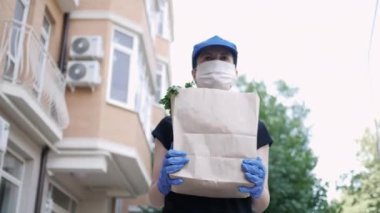 Kurye, koruyucu maskeli kurye ve tıbbi eldivenli teslimatçı paket yemek getiriyor. Karantina altında teslimat hizmeti, hastalık salgını, koronavirüs covid-19 salgını. Seçici odak