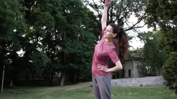 Mladá brunetka cvičí v městském parku. boční natáhnout před cvičením v parku — Stock video