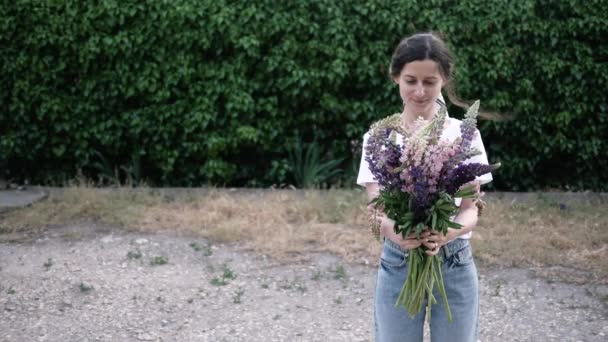 Genç kadın çiçeklere bakıyor, onları kokluyor ve gülümsüyor. Romantik bir kadın ve bir buket çiçek. Uzayı kopyala 4K — Stok video