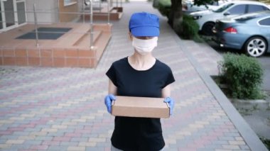 Lateks eldivenli ve tıbbi maskeli genç bayan teslimatçı karantina döneminde müşterilerine paket paketi ve malları teslim ediyor. Postacı.