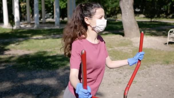 Konzept der sozialen Distanzierung. Porträt einer jungen Frau im Park beim Sport in Schutzhandschuhen und Gesichtsschutzmaske auf dem Laufband — Stockvideo