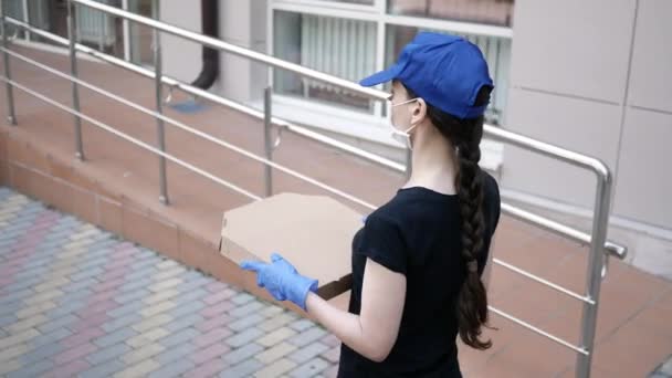 Entrega de alimentos jovem mulher bonita em máscara protetora e luvas carrega uma caixa de pizza de loja em casa. Homem de entrega de pizza durante a pandemia covid-19 — Vídeo de Stock