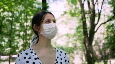 Park 'ta yeşil ağaçların arasında genç bir kadın var ve tıbbi koruyucu yüz maskesi ile derin bir nefes al.