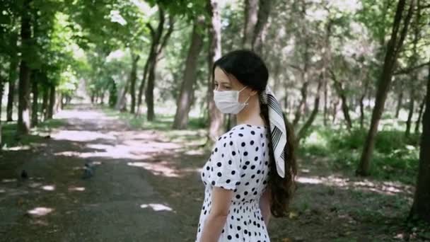 Красивая молодая женщина, гуляющая в парке летом в защитной маске для лица — стоковое видео