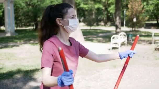 Νεαρή γυναίκα με προστατευτική μάσκα προσώπου και γάντια, πηγαίνει για σπορ σε υπαίθριο εξοπλισμό γυμναστικής στο πάρκο. Η έννοια της κοινωνικής απόστασης — Αρχείο Βίντεο