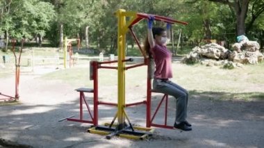 Eldivenli ve maske takan genç bir kadın Park 'taki spor aletlerinde. Halka açık yerlerde simülatör kullanımında koronavirüs salgınından korunma