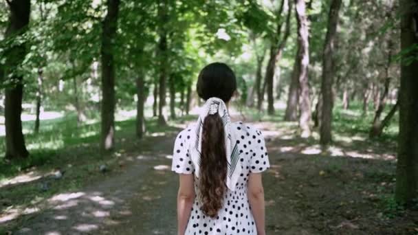 Giovane donna in abito bianco va a Park in estate, vista da dietro. Si gira per affrontare la macchina fotografica sulla sua maschera protettiva da un'allergia o un virus — Video Stock
