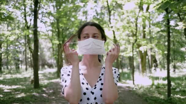 Young woman removes mask while nobody sees and puts on, she makes breath of fresh air in Park. concept of removing limitations of pandemic or end of Allergy — Stock Video