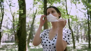 Güzel genç bir kadın koruyucu maskesini çıkartıyor. Alerjisi ya da virüsü dışarıda, parkta yüzünden çıkarıyor. Yakın çekim.