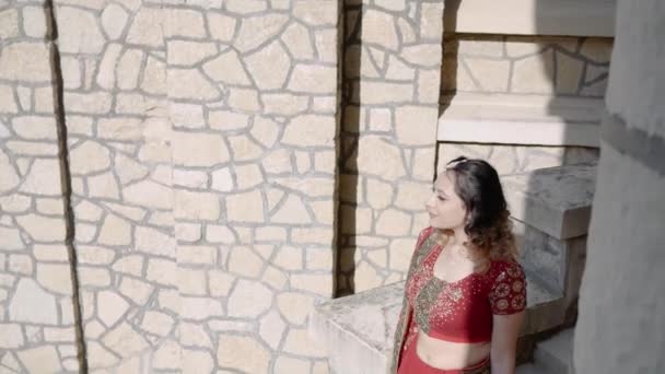 Belle Saree d'origine indienne. Jeune femme en tenue rouge, colorée, sensuelle, de mariage et très féminine - sari indien se promène le long des vieilles rues en Inde. Vêtements nationaux traditionnels des femmes indiennes — Video