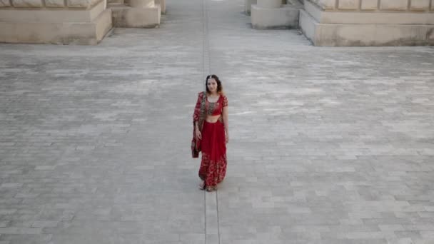 Joven hermosa mujer india camina por antiguas calles de arquitectura de la ciudad de la India vestida con sari rojo, decorada con adornos tradicionales y patrones Mehendi, dibujos de henna en las manos — Vídeos de Stock