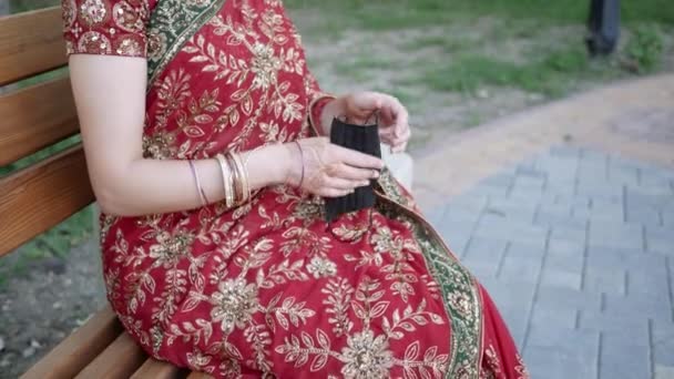 Ung kvinne i tradisjonelt indianerantrekk tar på seg ansiktsmaske i Park – stockvideo