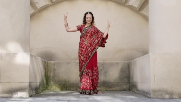 インドの女性は赤いサリを身に着けているインドの古代建築都市の通りで踊り、伝統的な装飾品やメフェンディのパターンで飾られています。 — ストック動画