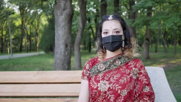 Young woman in traditional Indian outfit wears protective face mask on in Park — Stock Video