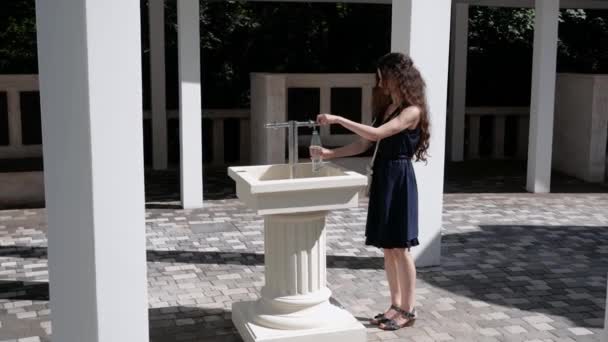 Giovane bella donna versando acqua minerale in una bottiglia alla fonte — Video Stock