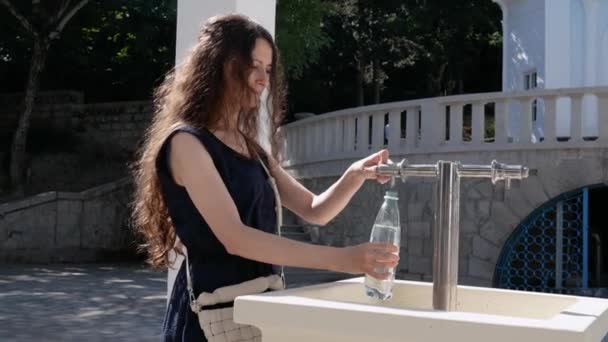 Mulher bonita nova derramando água mineral em uma garrafa na fonte — Vídeo de Stock