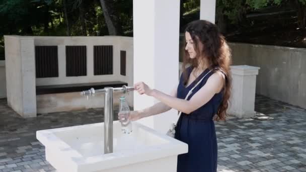 Sala pompe con acqua minerale all'aperto. giovane donna raccoglie acqua potabile in bottiglia dalla fonte — Video Stock