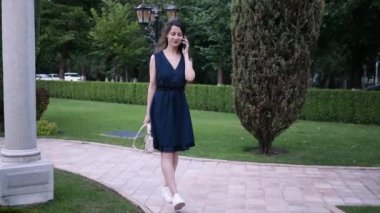 Genç esmer kadın yazın sokakta yürürken cep telefonuyla çağrıya cevap veriyor.