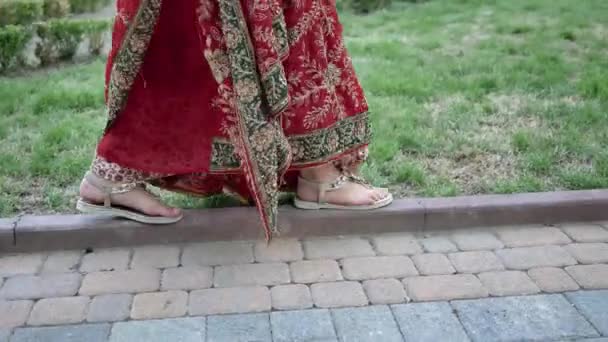 Gros plan de femme indienne pieds en sandales marchant dans les rues du parc de la ville de l'Inde vêtue de Sari rouge, décorée d'ornements traditionnels — Video