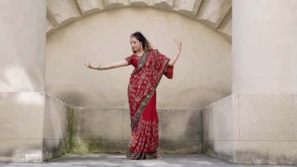 Νεαρή όμορφη Ινδή γυναίκα χορεύει στο κόκκινο Σάρι σε τοίχους φόντο αρχαίο κτίριο σε εξωτερικούς χώρους — Αρχείο Βίντεο