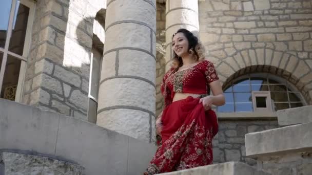 Genç ve güzel Hintli bir kadın şehrin antik mimari caddelerinde yürüyor. Kırmızı Sari giyinmiş, geleneksel süslemeler ve Mehendi desenleriyle süslenmiş. — Stok video