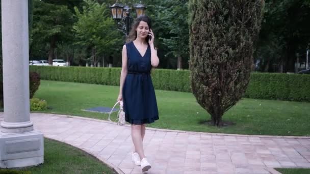 Jovem morena mulher responde chamada no celular andando rua abaixo no verão — Vídeo de Stock