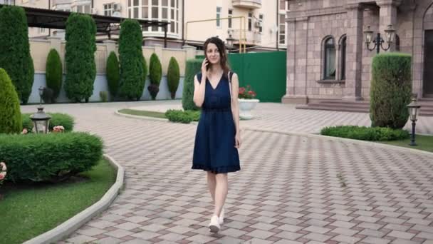 Jovem mulher bonita andando no vestido de verão marca o número de alguém e falando no telefone — Vídeo de Stock