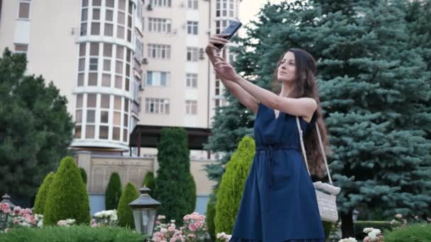 Young beautiful woman posing and taking pictures of herself in selfie camera phone in summer — Stock Video