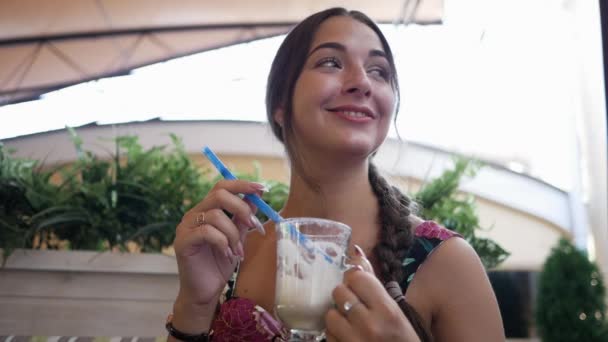 Junge hübsche Frau im Café lächelt und hält einen Cocktail mit einem Strohhalm in der Hand — Stockvideo