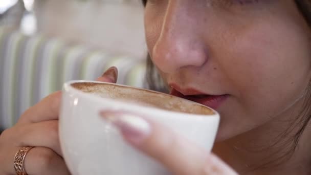 In einem Café trinkt eine junge Frau mit einer Tasse Kaffee — Stockvideo