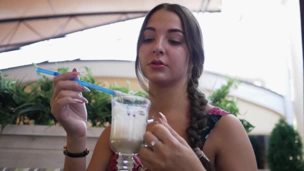 Junge hübsche Frau in einem Outdoor-Restaurant rührt ein Getränk mit einem Strohhalm und trinkt einen Cocktail aus einem Strohhalm — Stockvideo