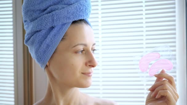 Giovane bella donna tiene in mano rosa collagene idrogel cerotti cosmetici sotto gli occhi. Ritratto di giovane donna felice sorridente e in posa per la pubblicità — Video Stock