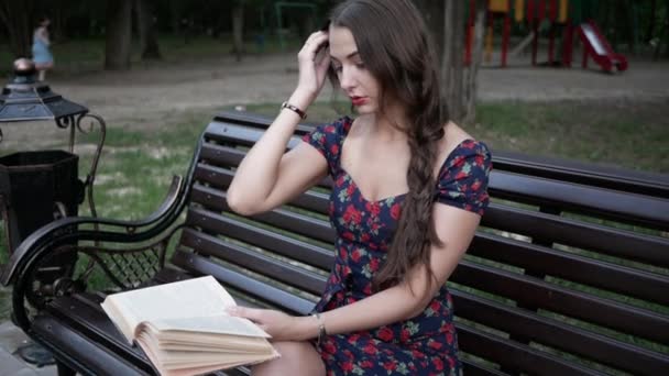 Giovane donna legge libro seduto da solo sulla panchina in estate Park, raddrizza i capelli — Video Stock