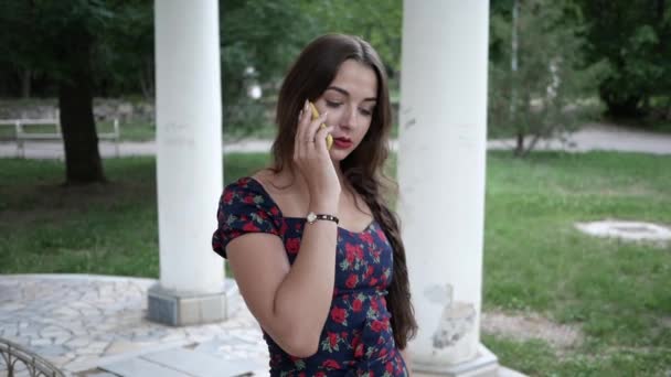 Schöne brünette Mädchen steht im Sommer Park beantwortet Anruf und Gespräche am Telefon — Stockvideo