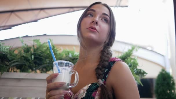 Joven mujer bonita en un café al aire libre posando con una bebida — Vídeo de stock