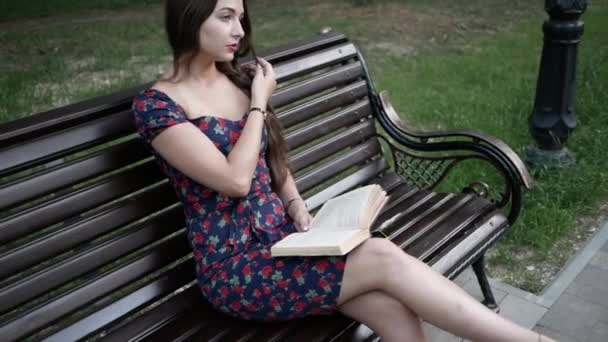 Giovane bella donna è seduta su una panchina a Park e la lettura di un libro — Video Stock