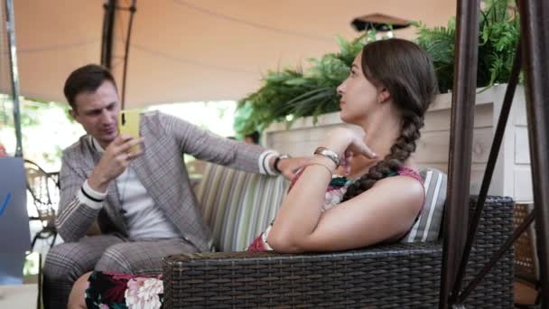 Hombre toma la foto con la cámara del teléfono hermosa joven sentada en la mesa en la cafetería — Vídeos de Stock