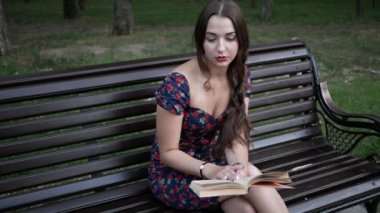 Genç ve güzel bir kadın parkta bir bankta oturuyor ve kitap okuyor.