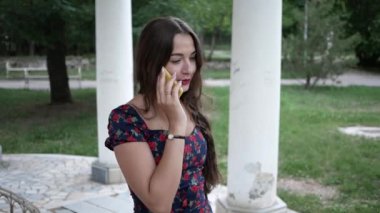 Genç esmer kadın telefonda konuşuyor. Yaz parkında gülümsüyor.