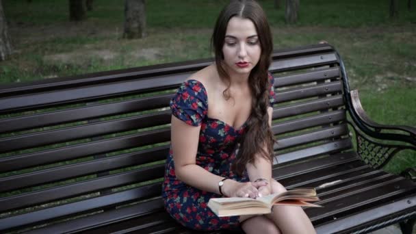 Giovane bella donna è seduta su una panchina nel parco e la lettura di un libro — Video Stock