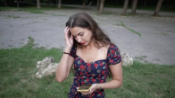 Jeune jolie femme utilise téléphone dans la rue dans le parc redresser ses cheveux — Video